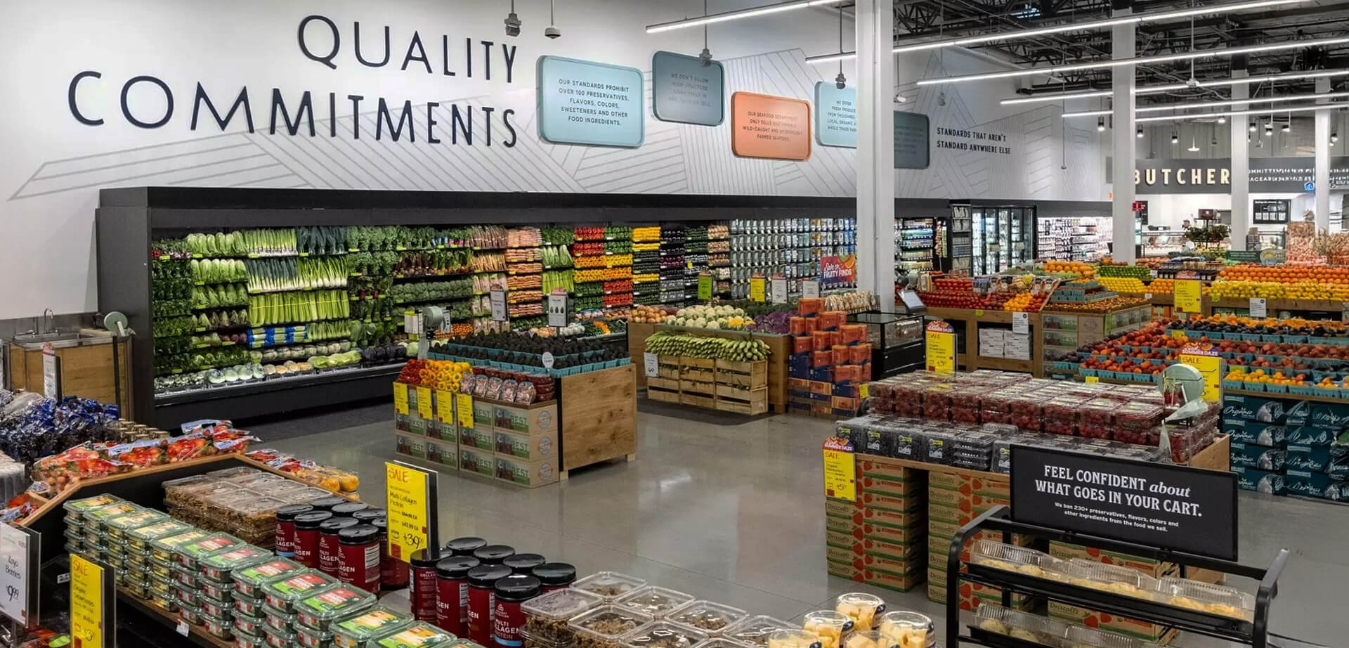 Whole Foods Market supermarket chain known for selling natural and organic food products.  The store environment is designed to be inviting and educational for customers.  The company emphasizes strict quality standards and a commitment to sustainable agriculture.  The text in the image highlights the store's "Quality Commitments" and encourages customers to "feel confident about what goes in your cart". 