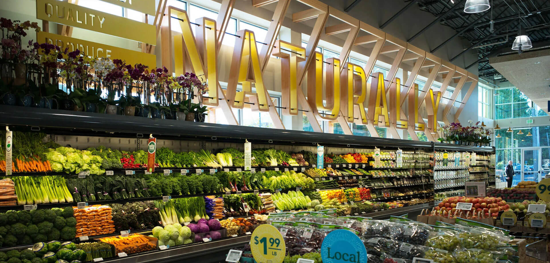 La tienda Whole Foods Market que se muestra en la imagen se encuentra en Eugene, Oregón, EE. UU. La señalización superior incluye las palabras "PRODUCTOS DE CALIDAD" y un gran cartel decorativo que dice "NATURALMENTE".