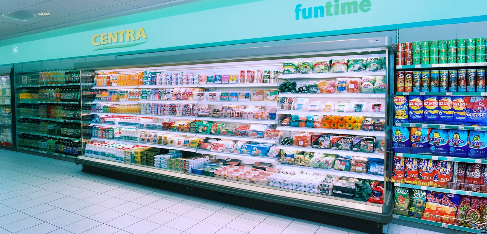 This image displays an interior view of a Centra convenience store, a retail brand primarily known in Ireland and Northern Ireland.  Centra is a major convenience store chain with numerous locations across Ireland, offering a variety of groceries and food-to-go options. The store in the image features a large refrigerated section stocked with items like fresh produce, ready meals, and dairy products.