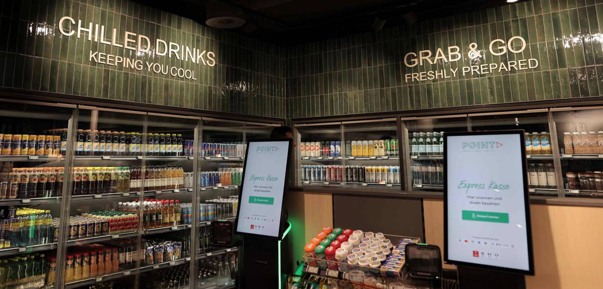 The image displays the interior of a SSP Point convenience store, which is tailored for travel locations. The store emphasizes speedy service through digital technologies like self-checkout systems and digital screens.  The store offers "Chilled Drinks" and "Grab & Go" freshly prepared items, as indicated by the wall signage.