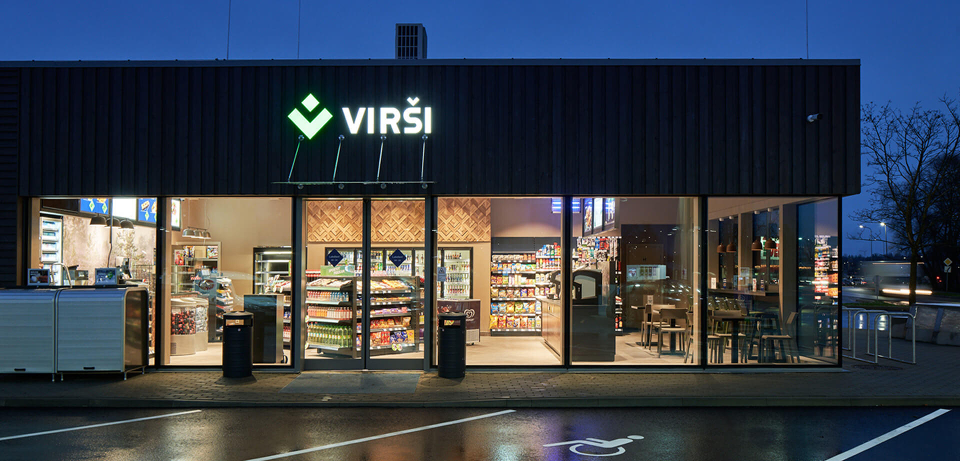The image shows a Virši service station, a prominent Latvian fuel and alternative energy trader that also operates a convenience store network. Convenience Store: The stations feature a convenience store and cafe area, often open 24 hours, offering a range of products including fresh food, snacks, coffee, drinks, and car products.