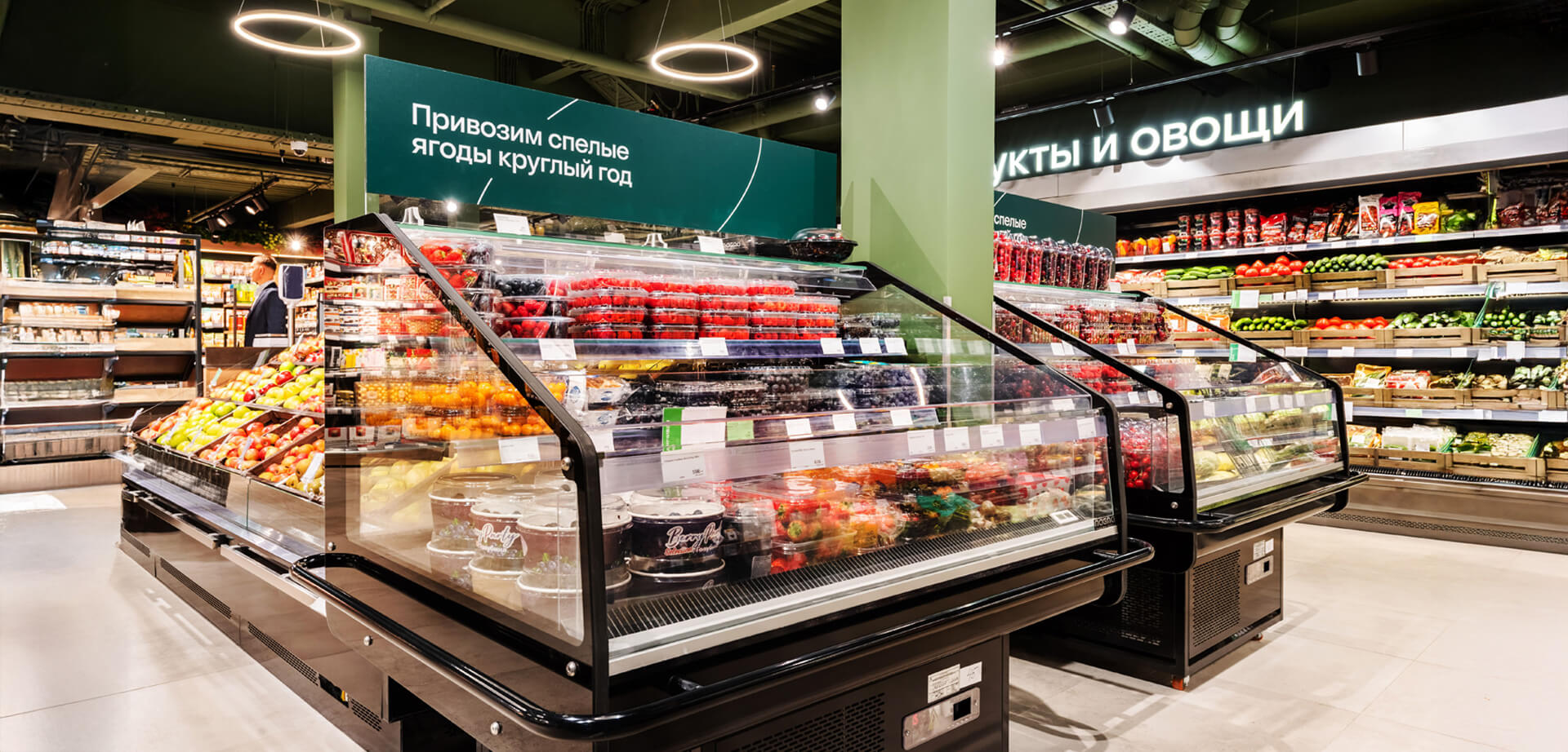 "Azbuka Vkusa" supermarket, a Russian retail chain known for high-quality food. The text on the signs indicates that the store offers ripe berries and other fruits and vegetables year-round. 