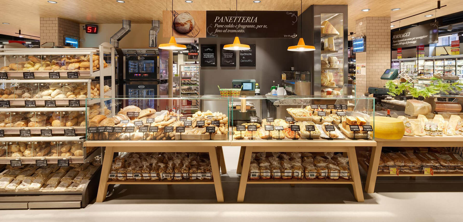 The image displays the interior of a Carrefour Market “Gourmet” store in Italy, specifically the bakery and cheese sections. The text on the signs indicates: PANETTERIA (Bakery) "Pane caldo e fragrante, per te, fino al tramonto" (Hot and fragrant bread, for you, until sunset) FORMAGGI (Cheese)