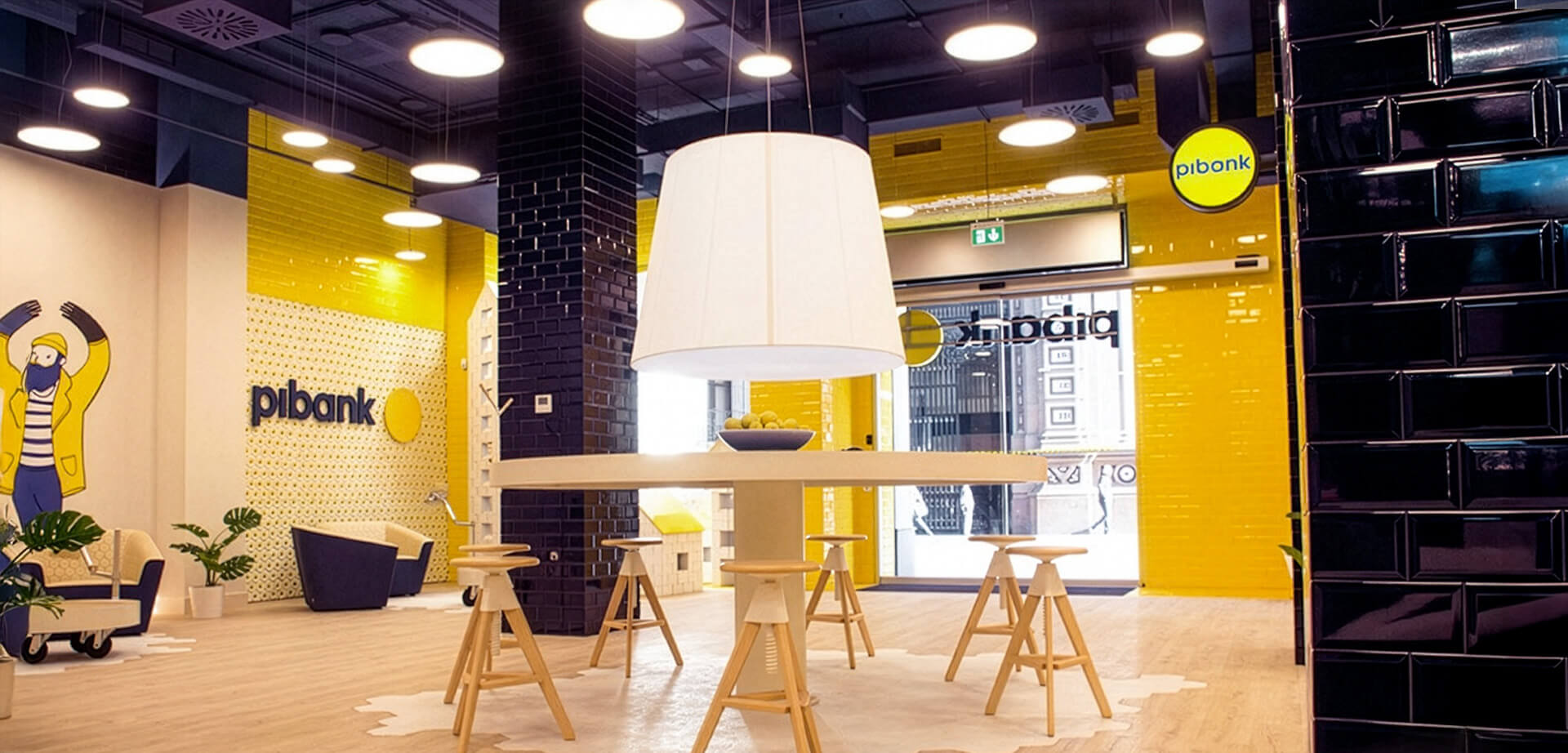 The image shows the interior of a Pibank branch office. Key details about the bank include:  Pibank is a digital bank brand that belongs to the Pichincha banking group, a multinational group from Ecuador.  It operates in several locations, including Spain and the USA. 