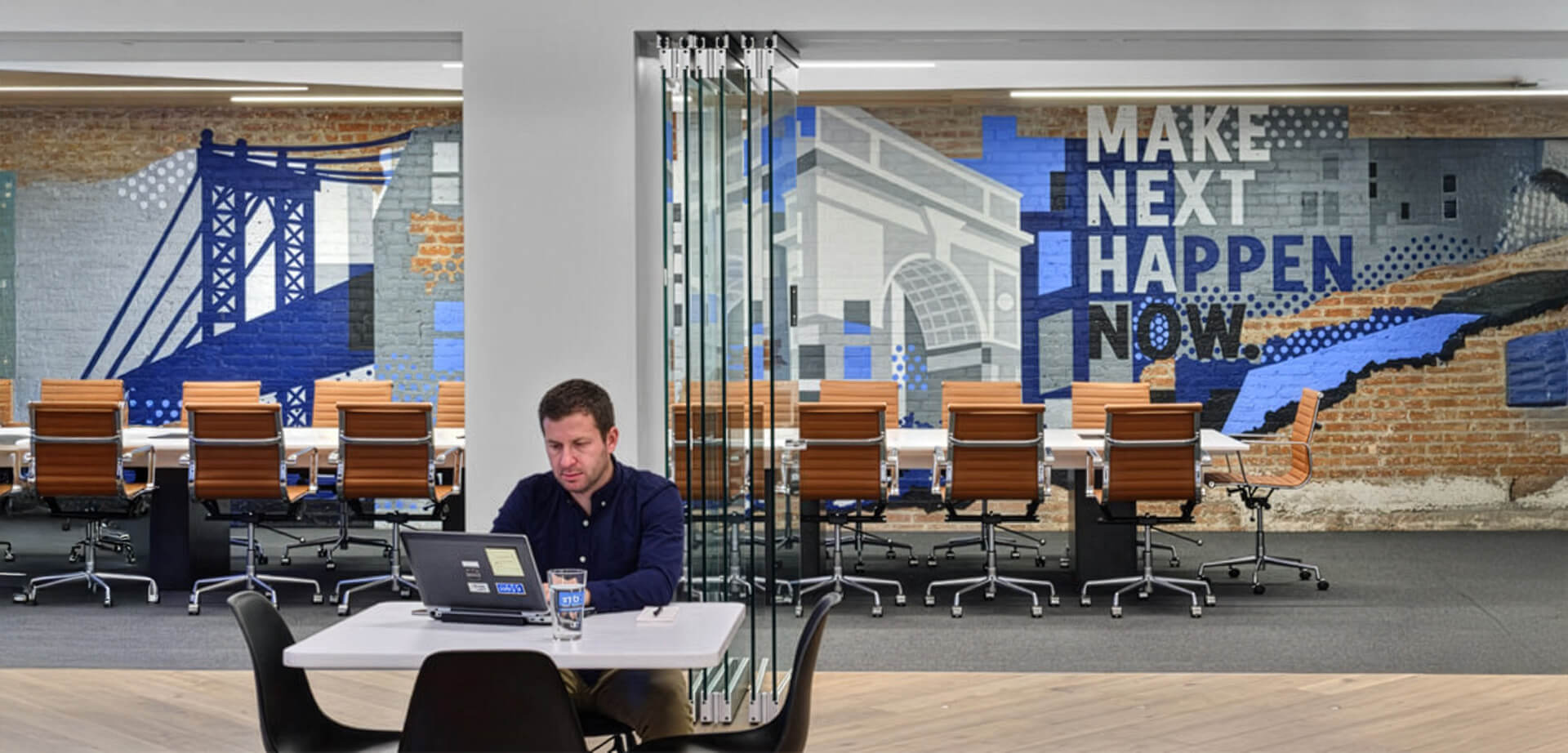 An office space with a prominent wall mural featuring the text, "MAKE NEXT HAPPEN NOW." This is a conference room in the Silicon Valley Bank (SVB) corporate office in New York City. 