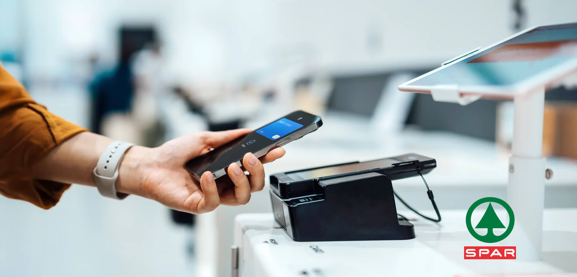 Ein Smartphone ermöglicht eine kontaktlose Zahlung an einem Kassenterminal, wahrscheinlich in einem SPAR-Laden.