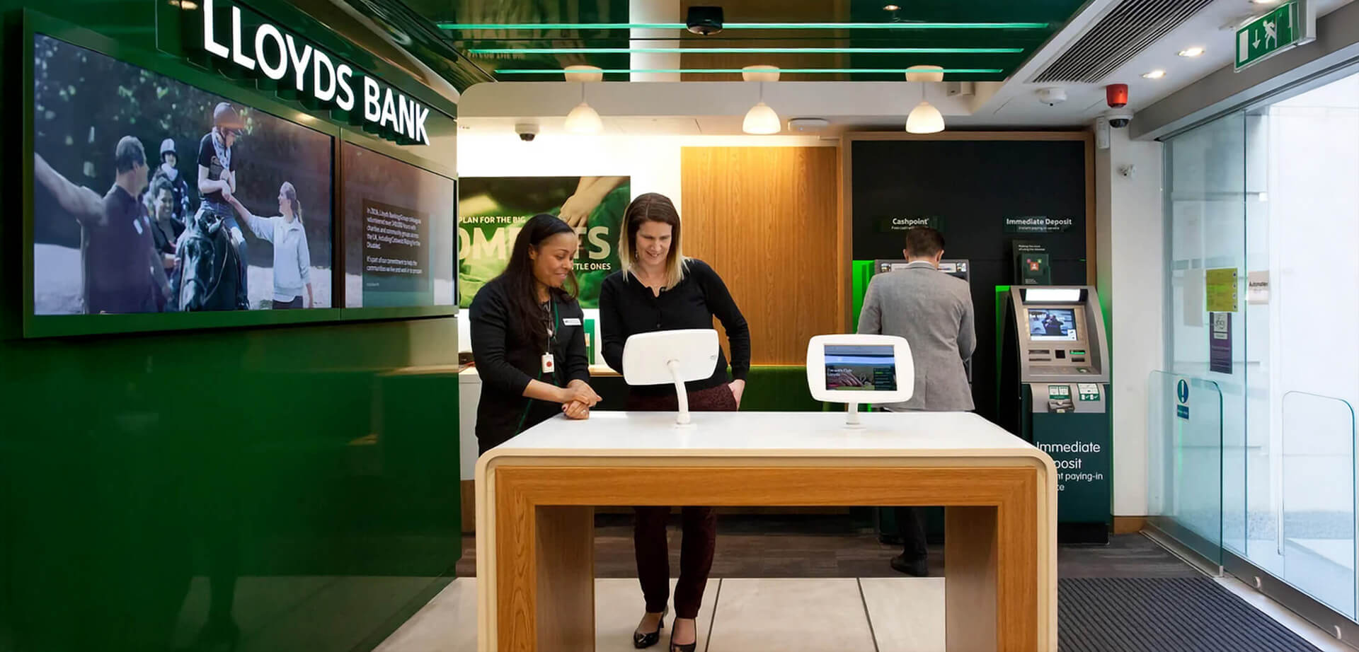 The interior of a modern Lloyds Bank branch in the UK.  It features a "phygital" design, combining physical space with digital self-service tools. 