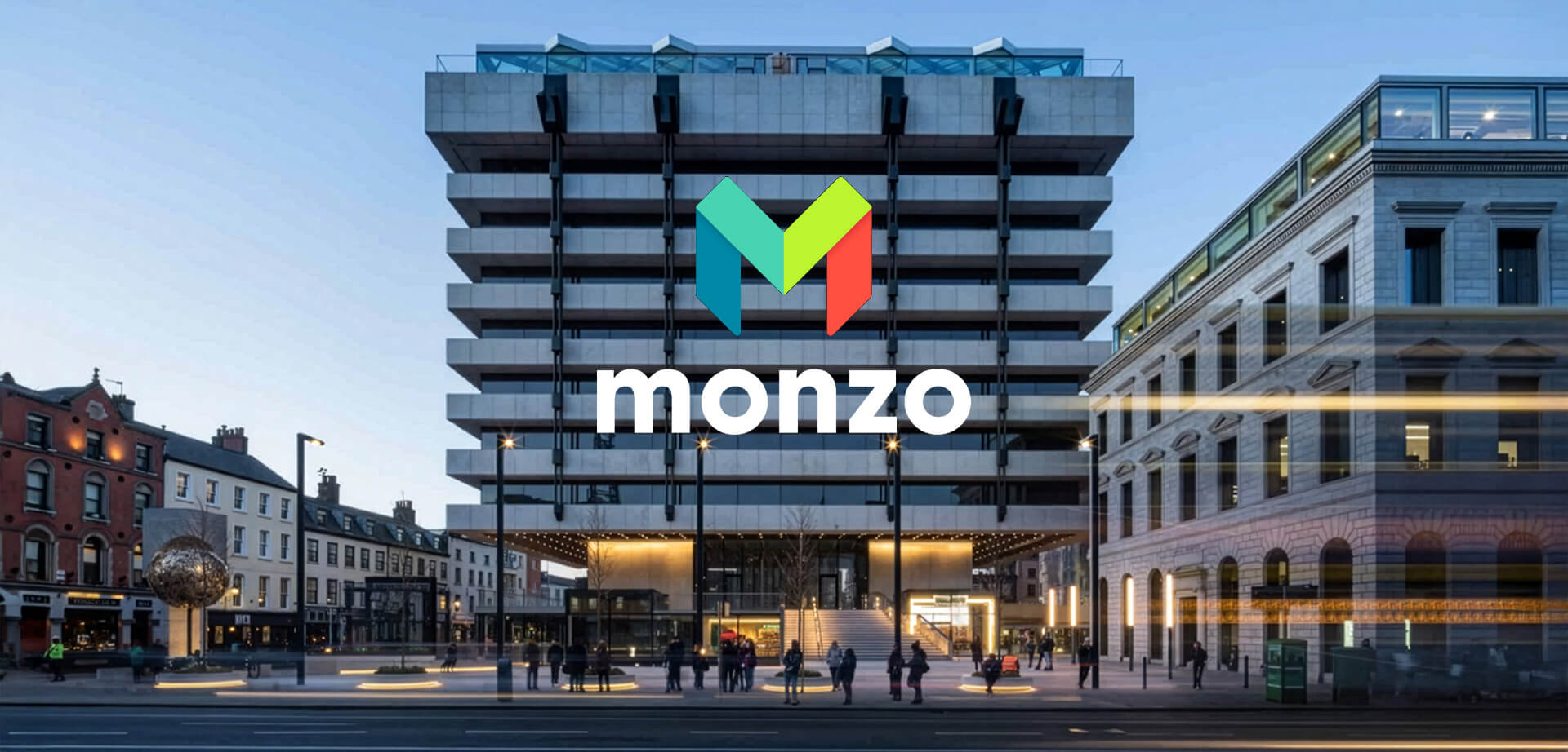 The image displays the Monzo logo superimposed onto a building in a city center plaza, which appears to be a digital manipulation rather than a physical sign. 