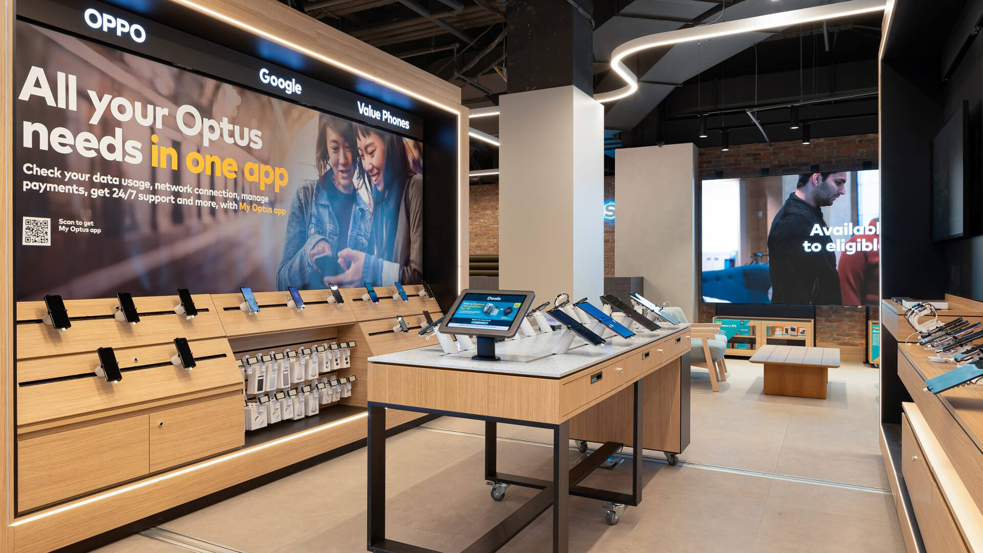 This is an interior view of an Optus retail store featuring modern wooden fixtures and interactive display tables.