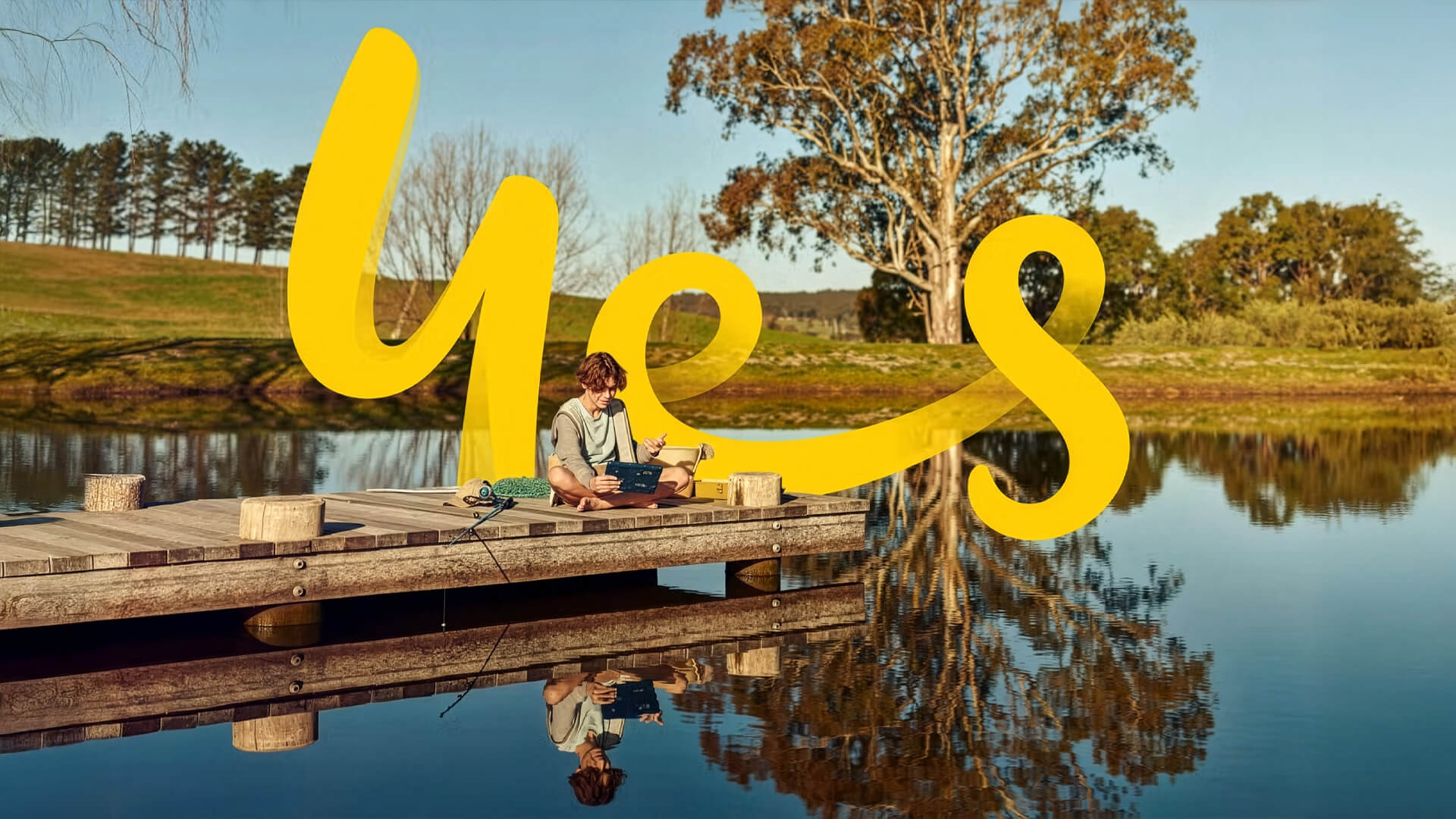 A brand refresh for Optus, featuring a stylized yellow "yes" script overlaid on a tranquil outdoor scene