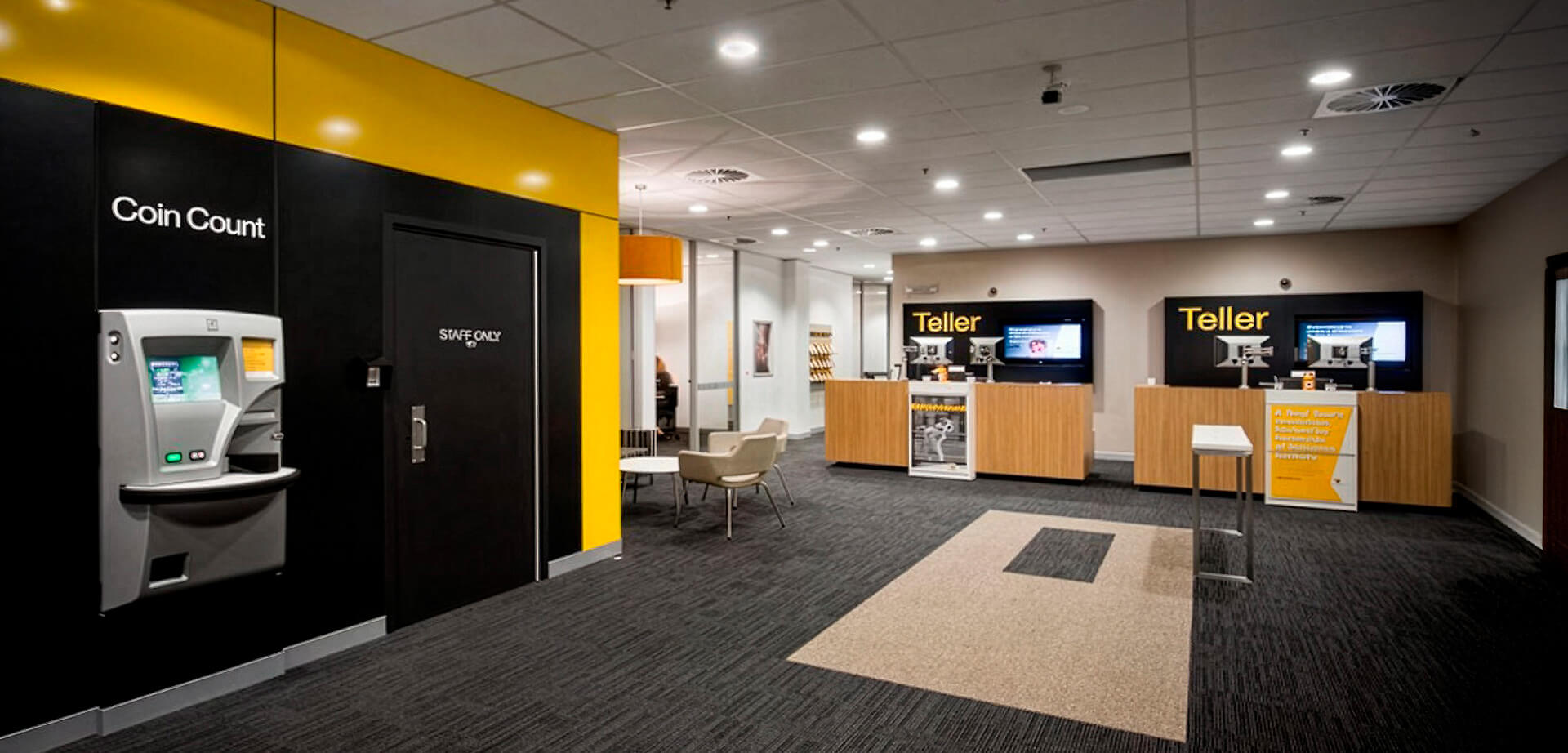 A modern bank branch, featuring a prominent coin-counting kiosk, teller stations, and a staff-only area. Combines digital self-service with traditional in-person assistance to offer more flexible financial services.