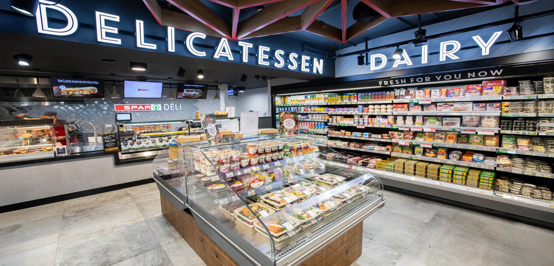 This image shows the interior of a modern SPAR Deli and Dairy section, which is part of an international retail chain originally founded in the Netherlands. The store has been updated to focus heavily on fresh, ready-to-eat foods.