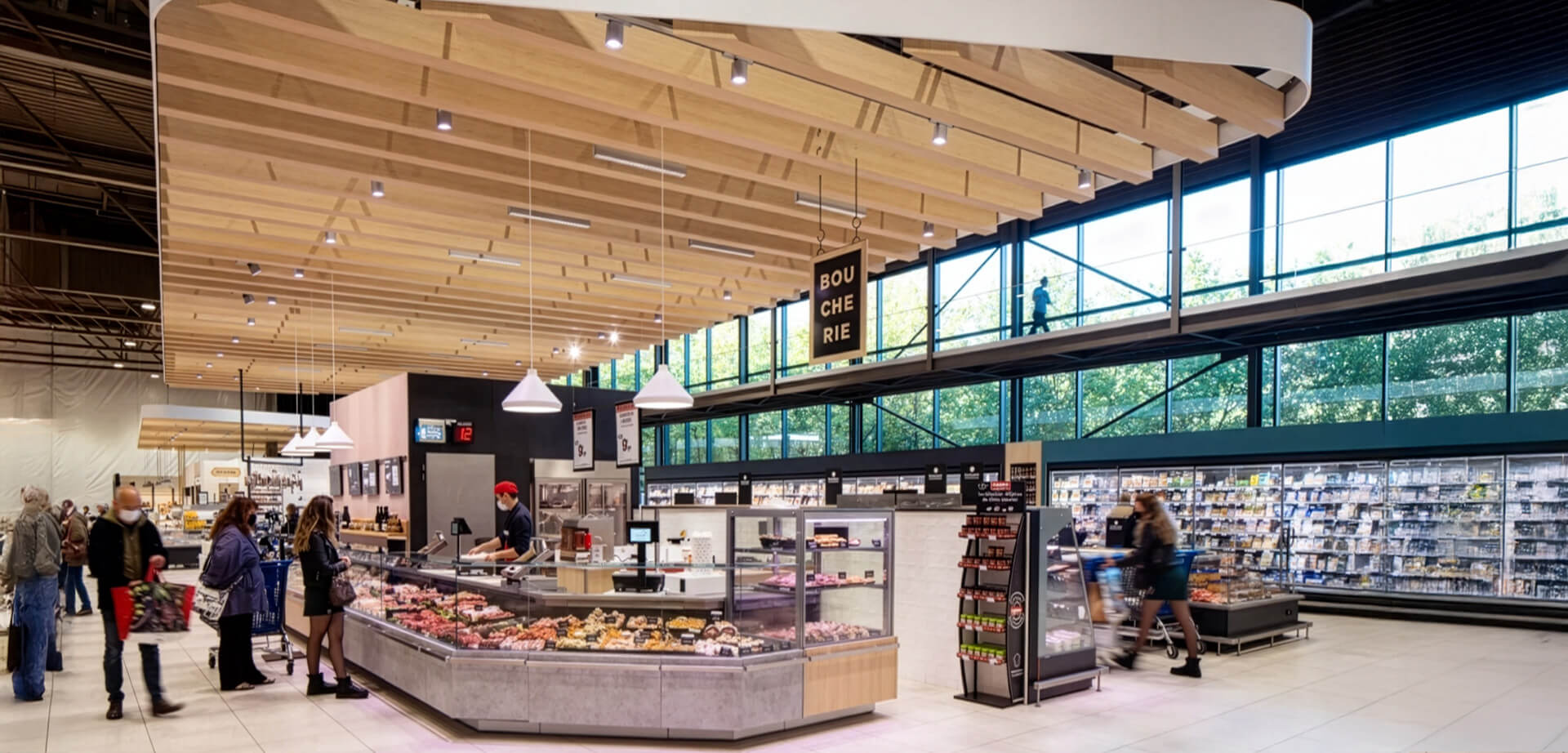 The image shows the butcher (boucherie) counter at the E.Leclerc hypermarket in La Roche-sur-Yon, France. The store underwent a sustainable redesign focused on natural light, warm wood paneling, and biophilic principles rather than traditional, sterile supermarket aesthetics.
