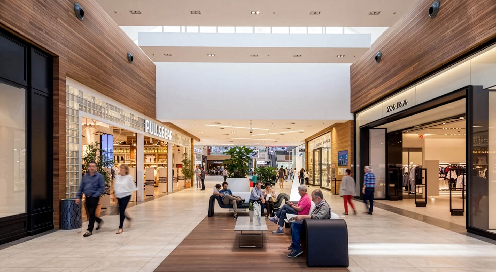 This image shows the bright, modern interior corridor of the Centro Comercial Garbera shopping center in San Sebastián, Spain, featuring high wooden-paneled walls, seating areas, and storefronts.