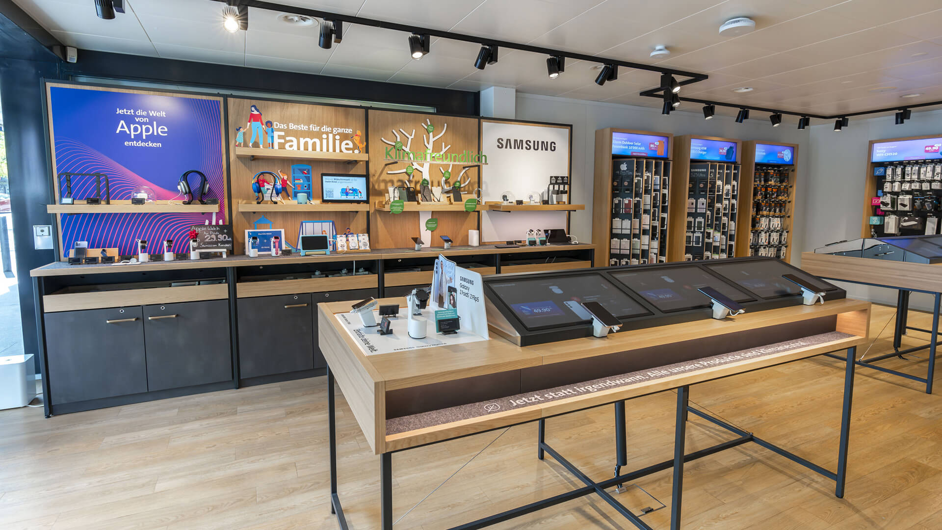 The image shows the interior of a retail telecommunications store, a Swisscom Shop, featuring dedicated brand display sections for Apple and Samsung with interactive product tables and wall fixtures.