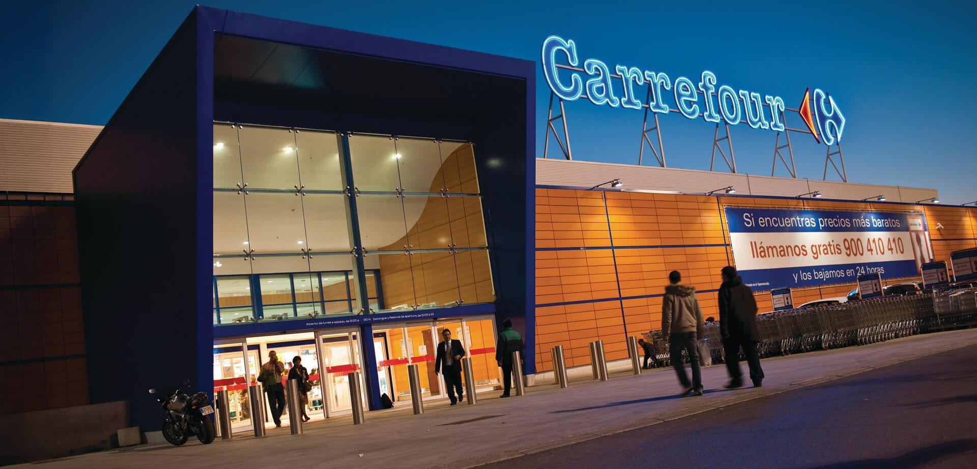 A Carrefour Hypermarket. The architecture features a striking blue geometric entrance structure juxtaposed against vibrant orange wall paneling.