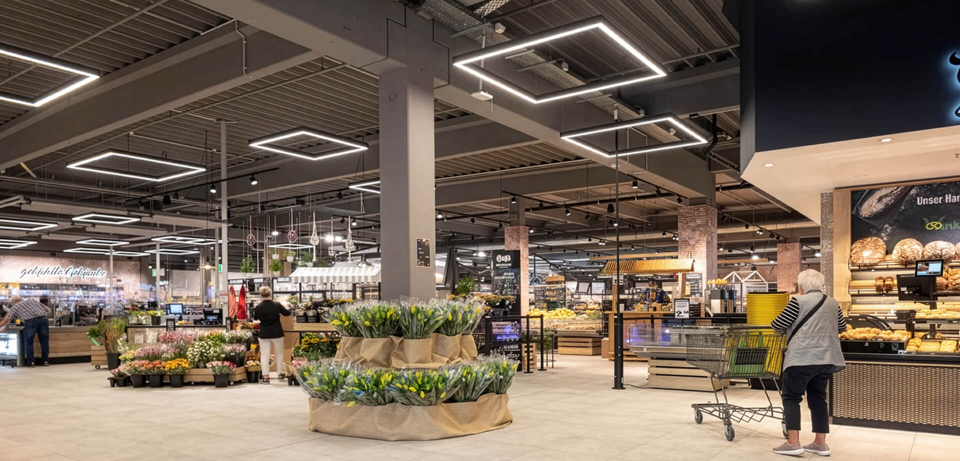 Edeka Massak, store interior featuring a floral display in the center and a bakery counter on the right.